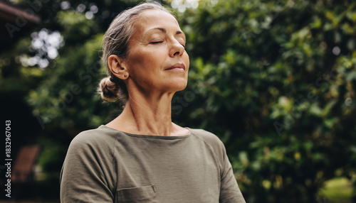 Close up portrait of a senior woman with eyes closed meditating and breathing deeply in a green outdoor garden