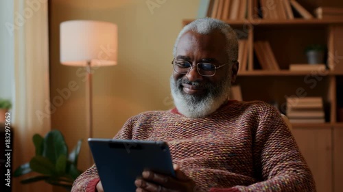 Elderly man enjoys reading on tablet in cozy living room while relaxing in comfortable chair with smile and joy