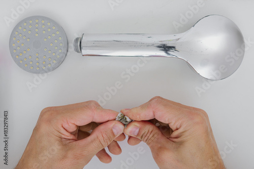 Male plumber fixing bathroom showerhead, closeup photo. Squeezing used shower filter after water cleaning, close-up