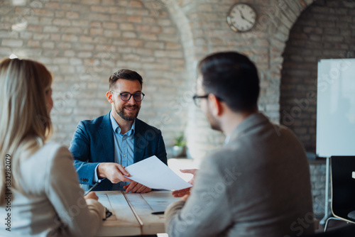 Bild auf Leinwand Three business professionals sitting at a table in a modern office, engaged in a lively conversation