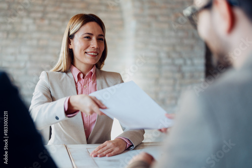 Φωτογραφία A female manager is passing a report or agreement paperwork to a male employee across a desk in a modern office setting, discussing business details