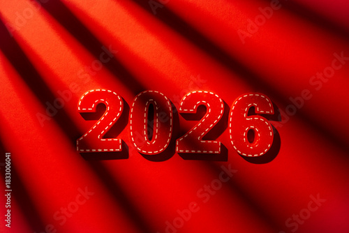 Red felt numerals for the year 2026 lie on a vibrant red background, bathed in diagonal sunlight creating strong shadows, symbolizing future dates and upcoming New year concepts
