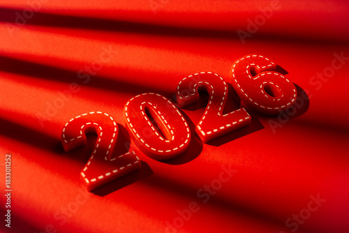 Red wooden numbers 2026 are sitting on a vibrant red background with abstract shadows, representing the upcoming calendar year, new beginnings, future planning, and milestones