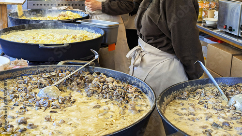 Aromatic mushroom stew simmers in large pans at an outdoor culinary event. Cooks serve this flavorful dish, offering a hearty experience for all attendees. 