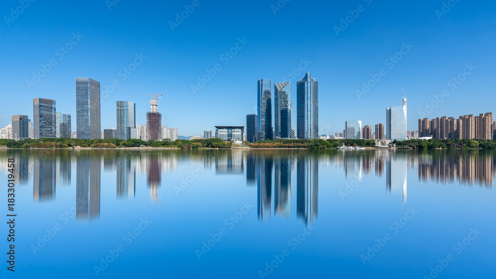 Fototapeta premium Modern city skyline with calm water reflection under clear blue sky