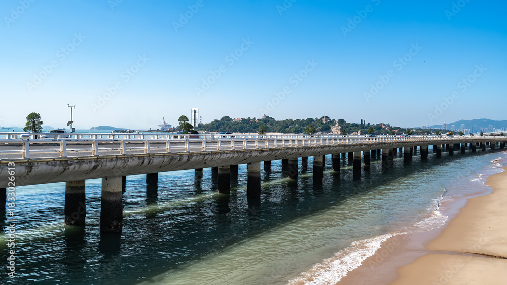 Obraz premium Long bridge extending over calm water near sandy beach