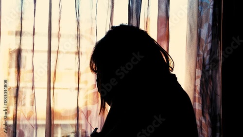 A woman is seen in silhouette, head bowed near a window with sheer curtains and warm sunset light, evoking a sense of sorrow or emotional distress.