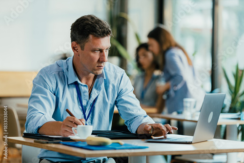 Young Professional Preparing for Meeting in Modern Office Cafe with Laptop and Notes