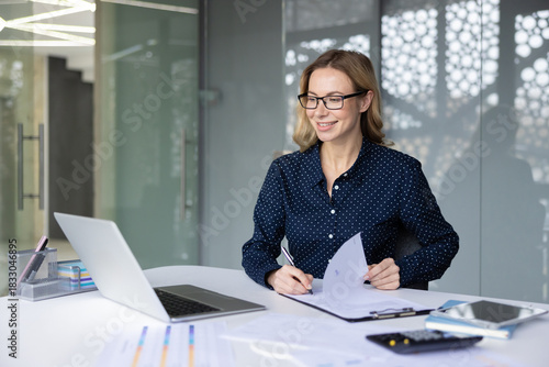 Bilde på lerret Smiling businesswoman in glasses completing financial paperwork at her modern of