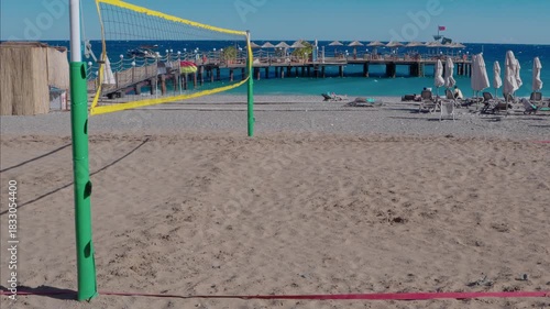 An empty volleyball court on a resort beach comes alive in the breeze, where the net gently sways, creating an atmosphere of tranquil anticipation. Golden sand lapped by the nearby sea and the gentle 