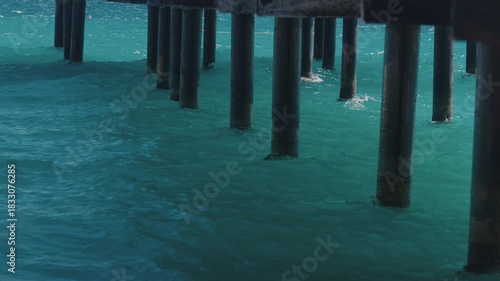The seawater swirls and splashes beneath the wooden pier deck, creating a rhythmic sound of waves against the pilings. 