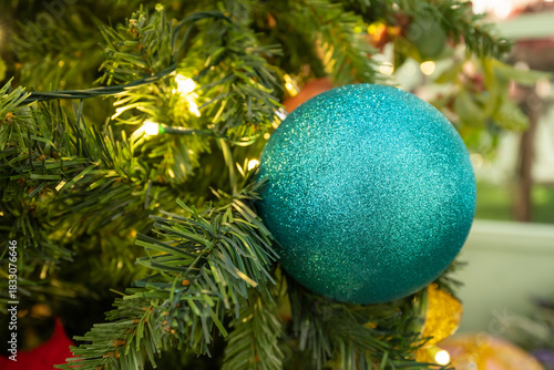 A bright turquoise glitter ball ornament adorns a green Christmas tree, capturing festive warmth and seasonal decoration.