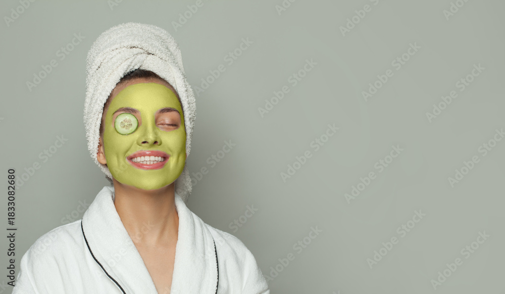 Fototapeta premium Portrait of young woman in green organic cosmetic face mask holding cucumber slices