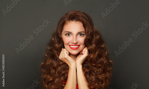 Smiling fashion model woman with shiny skin, wavy hairstyle and red lips makeup on black background