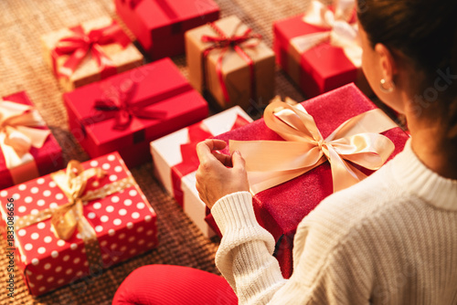 Over-the-shoulder view of woman preparing holiday gifts in red festive atmosphere