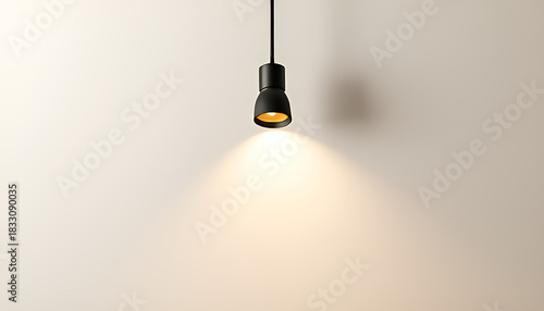 A single modern black pendant light hangs from a cord casting a warm focused beam of light onto a textured off white wall