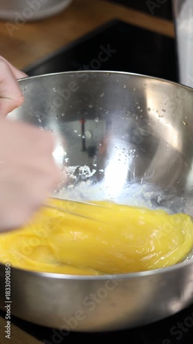 Close-up of hands whisking a rich yellow batter in a stainless steel bowl. Smooth, fast mixing creates a silky texture, capturing the satisfying, aesthetic rhythm of home cooking in motion