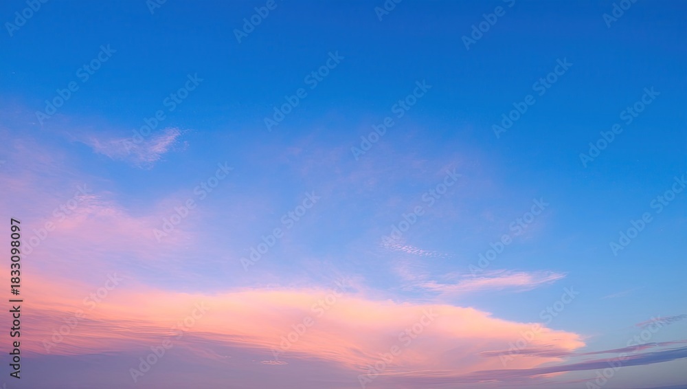 Fototapeta premium Pastel pink and orange clouds against deep blue sky at sunset or sunrise creating soft gradient atmospheric scene