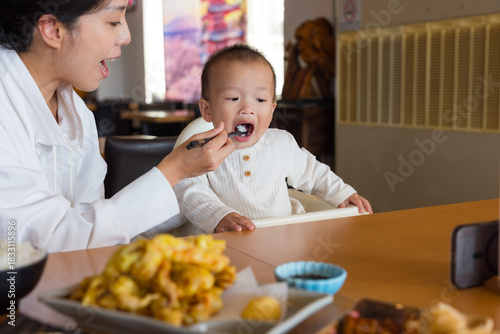 Young mum helping her son eat inside modern restaurant