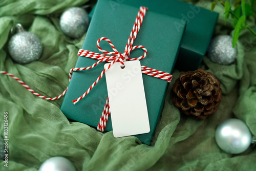 Blank white tag with dark green gift box on green fabric background, Christmas-themed mockup with clipping paths