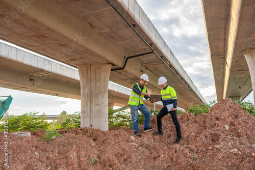 Construction workers collaborate on project under elevated highway urban area photography daylight close-up teamwork