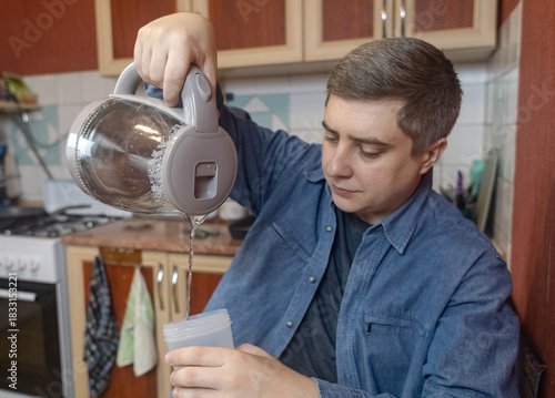 Man preparing a protein shake in a kitchen, measuring powder into a shaker for fitness, recovery, and muscle health.