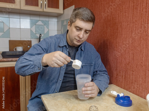 Man preparing a protein shake in a kitchen, measuring powder into a shaker for fitness, recovery, and muscle health.