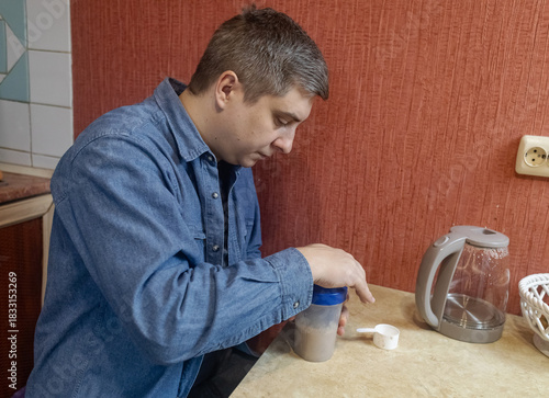 Man preparing a protein shake in a kitchen, measuring powder into a shaker for fitness, recovery, and muscle health.