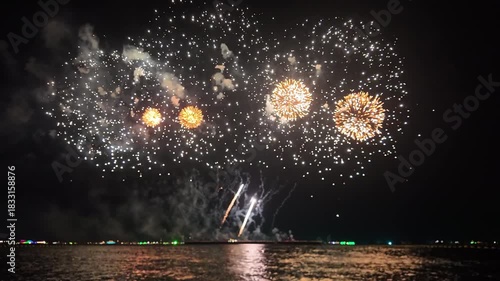 A spectacular fireworks display fills the night sky above water celebrating Christmas or New Year 