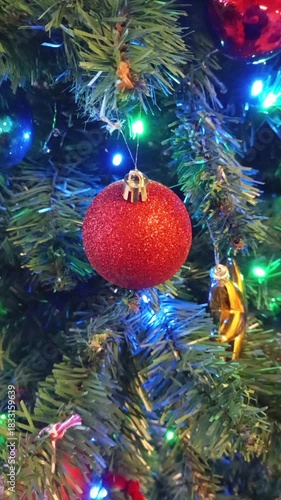 Close up of a decorated Christmas tree with sparkling red, blue, and gold ornaments, while yellow and blue lights blink softly, creating a festive and warm holiday atmosphere