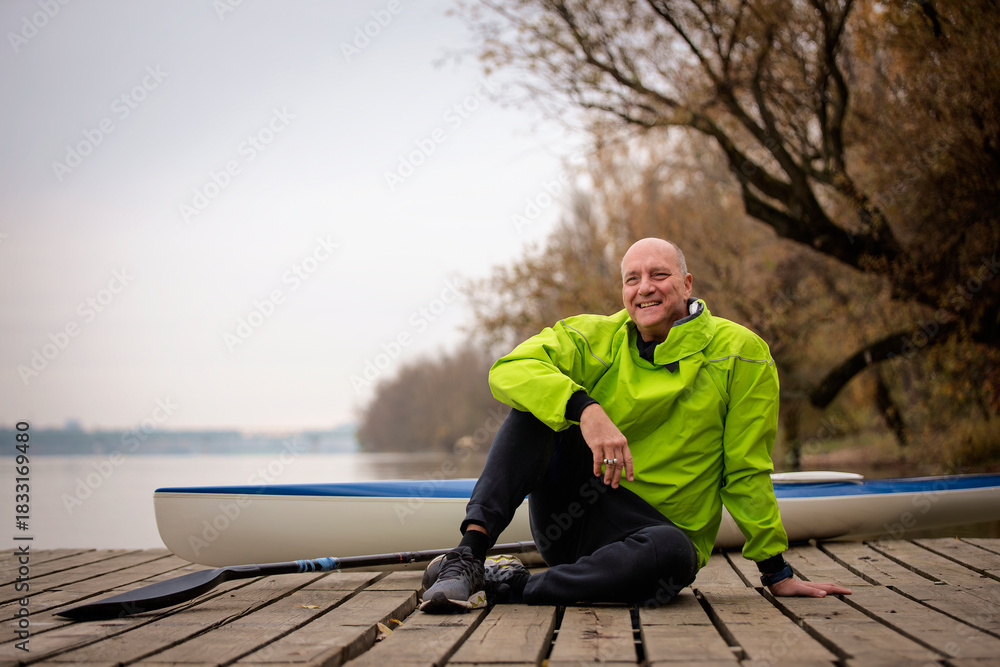 Fototapeta premium Sporty active senior man sitting on the jetty by the river next to his kayak