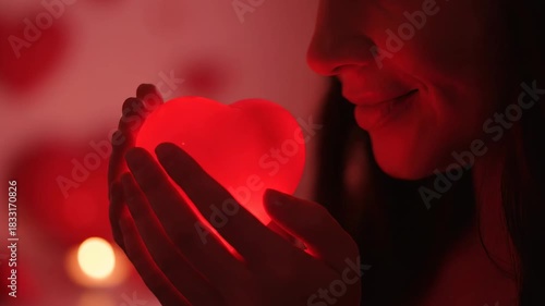 A woman smiling at a glowing red heart in her hands