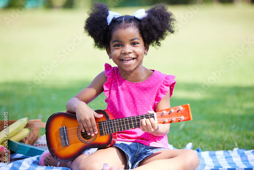 A girl playing ukulele outdoors in a park