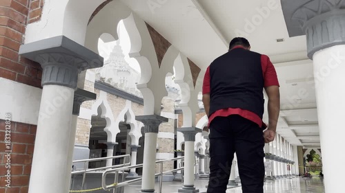 Anonymous man kneels in prayer inside the serene marble corridor of Masjid Jamek Sultan Abdul Samad in Kuala Lumpur, surrounded by arches and white columns