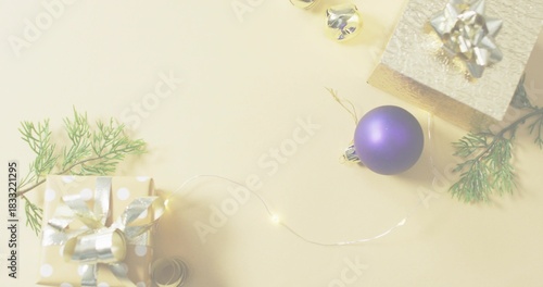 Styling flatlay with matte purple bauble on beige tabletop, wrapped gifts, fairy lights, copy space