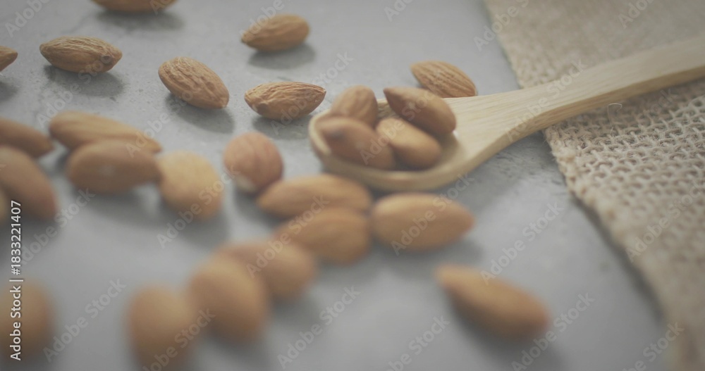 Obraz premium Displaying wooden spoon holding whole almonds on gray stone slab, burlap cloth nearby