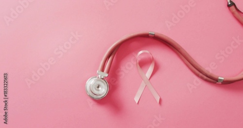 Displaying pink stethoscope and awareness ribbon lying on pastel pink surface, silver chest piece