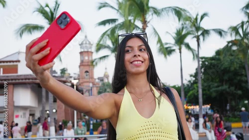 Young woman taking a selfie with smartphone smiling in a vibrant mexican city environment