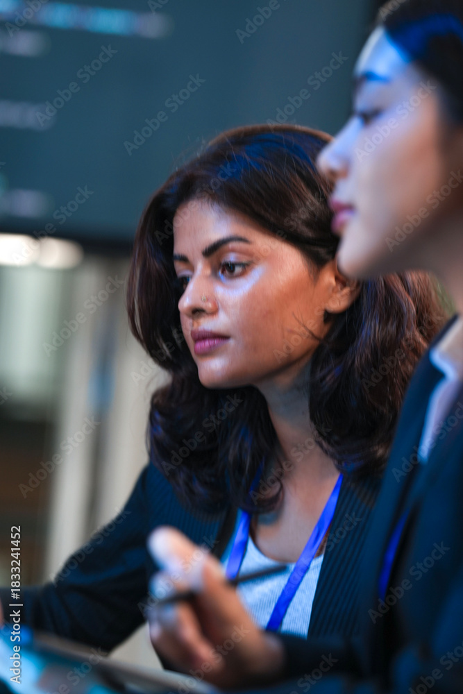 Fototapeta premium Close up profile intense focus. Young female professional deeply concentrates looking down colleague blurred foreground modern office environment serious contemplation moment captured quiet.