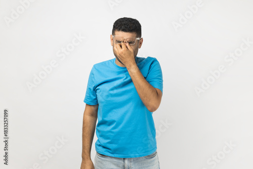 Tired exhausted unshaven man takes off his spectacles, rubbing his eyes, feels pain being overworked