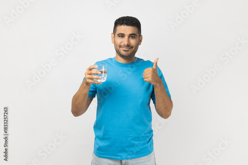 Positive man holding glass with water, recommend to drink at fresh clean water, showing thumb up.