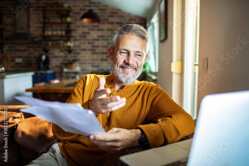 Obraz na płótnie Mature man smiling on video call with paperwork at home