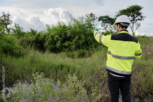 Environmental engineer wearing safety gear collecting water sample from polluted pond for contamination analysis, environmental testing, and ecological impact assessment in natural outdoor setting.