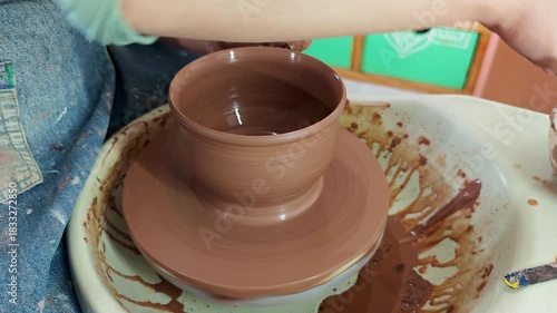 A person shaping clay on a pottery wheel, focusing intently on creating a ceramic piece with skillful hands.
