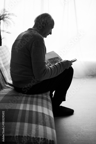 Fotografia Lonely elderly widower sitting on couch, holding old photos and recalling memories of his deceased wife
