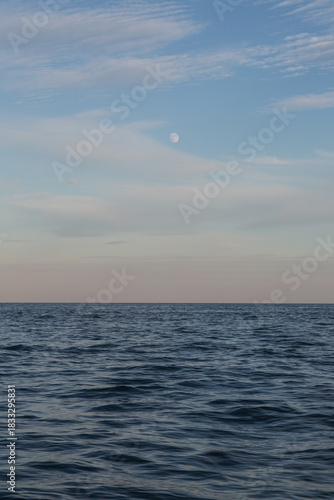 Sunset at the sea with the rising moon above the cloudy sky