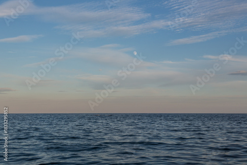 Sunset at the sea with the rising moon above the cloudy sky