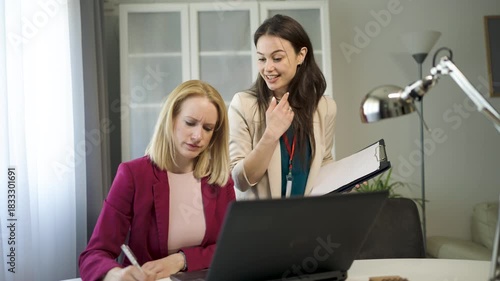 Two young women work from home side by side, each focused on her laptop in a cozy domestic environment.