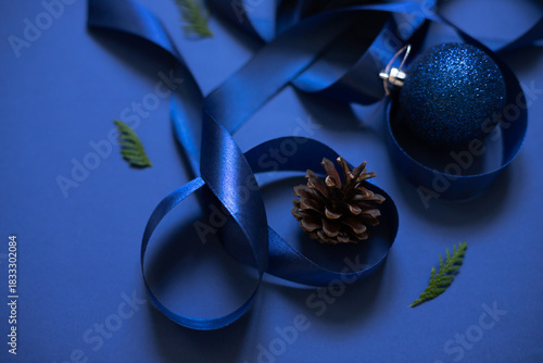Christmas celebration concept monochrome color composition with satin ribbon and festive baubles on the blue background