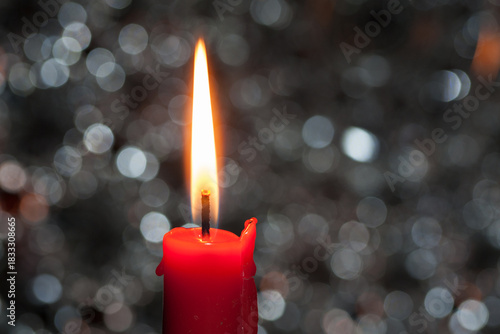 A red candle burns softly, surrounded by shimmering silver bokeh lights – an elegant, festive motif perfect for holiday editorials and magazine covers.